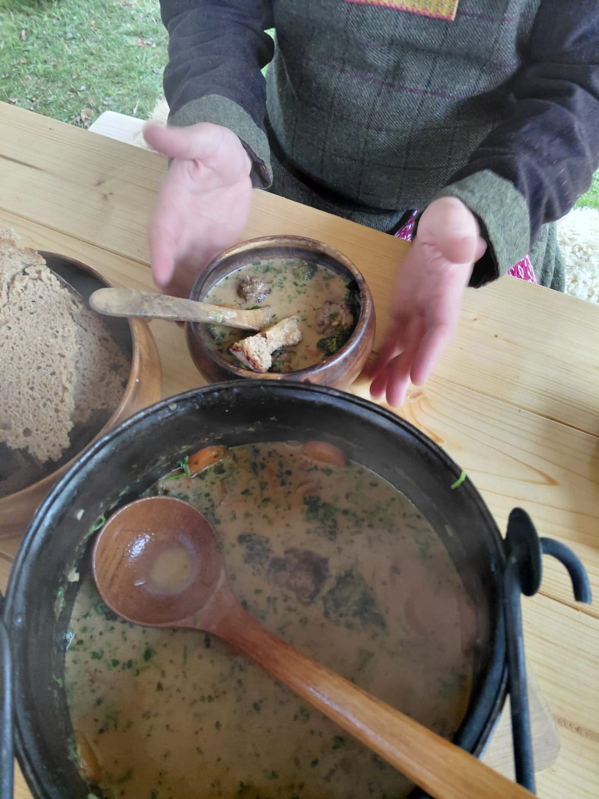 Frisch ausgeschenkt: Eintopf in der Holzschale, dazu Brot — dahinter der Eisenkessel mit Holzkelle