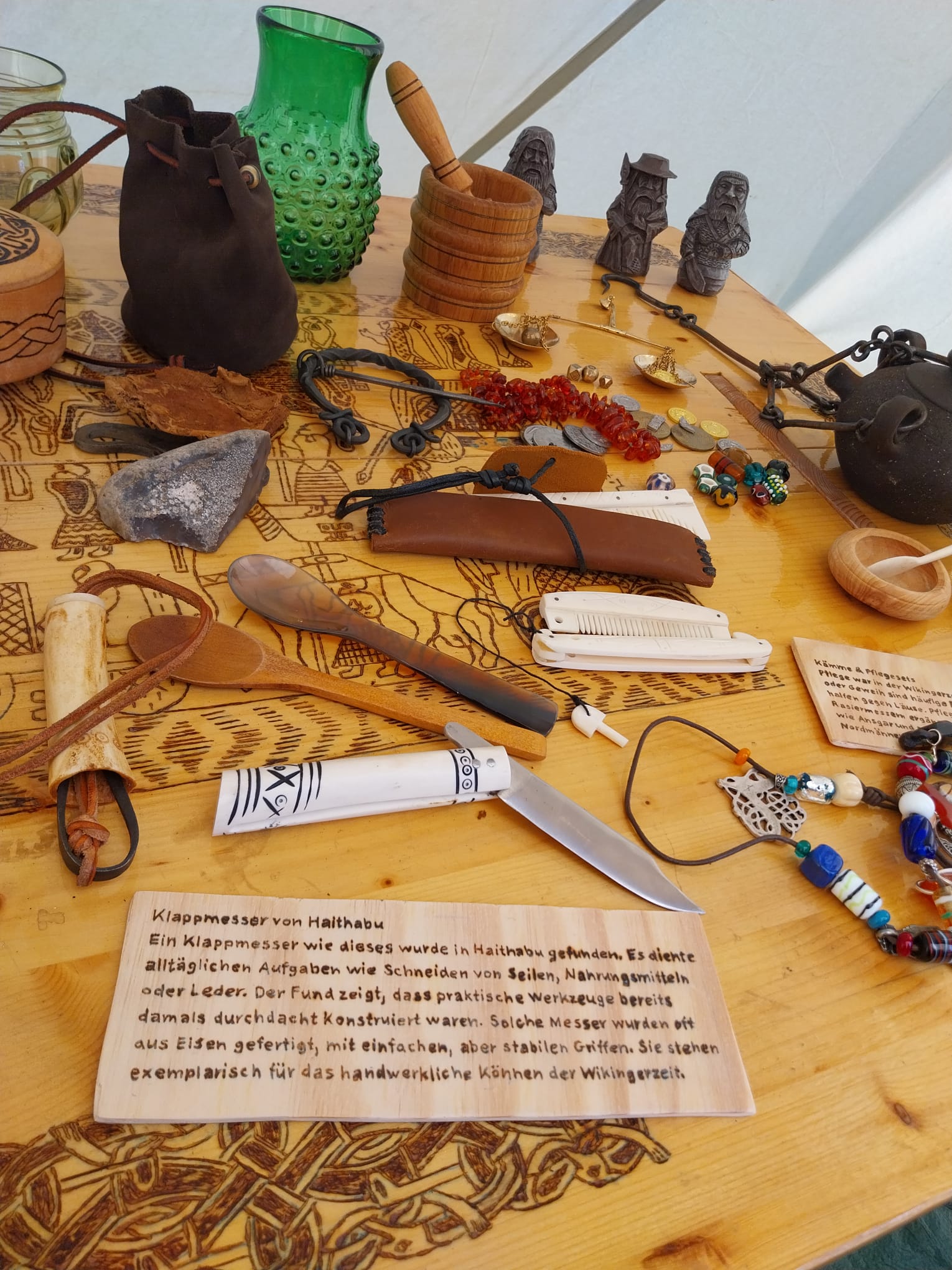 Im Museumszelt: Ausstellungstisch mit Glas, Keramik, Spielfiguren, Kämmen, Schmuck und Perlen — jedes Stück mit Erklärtäfelchen