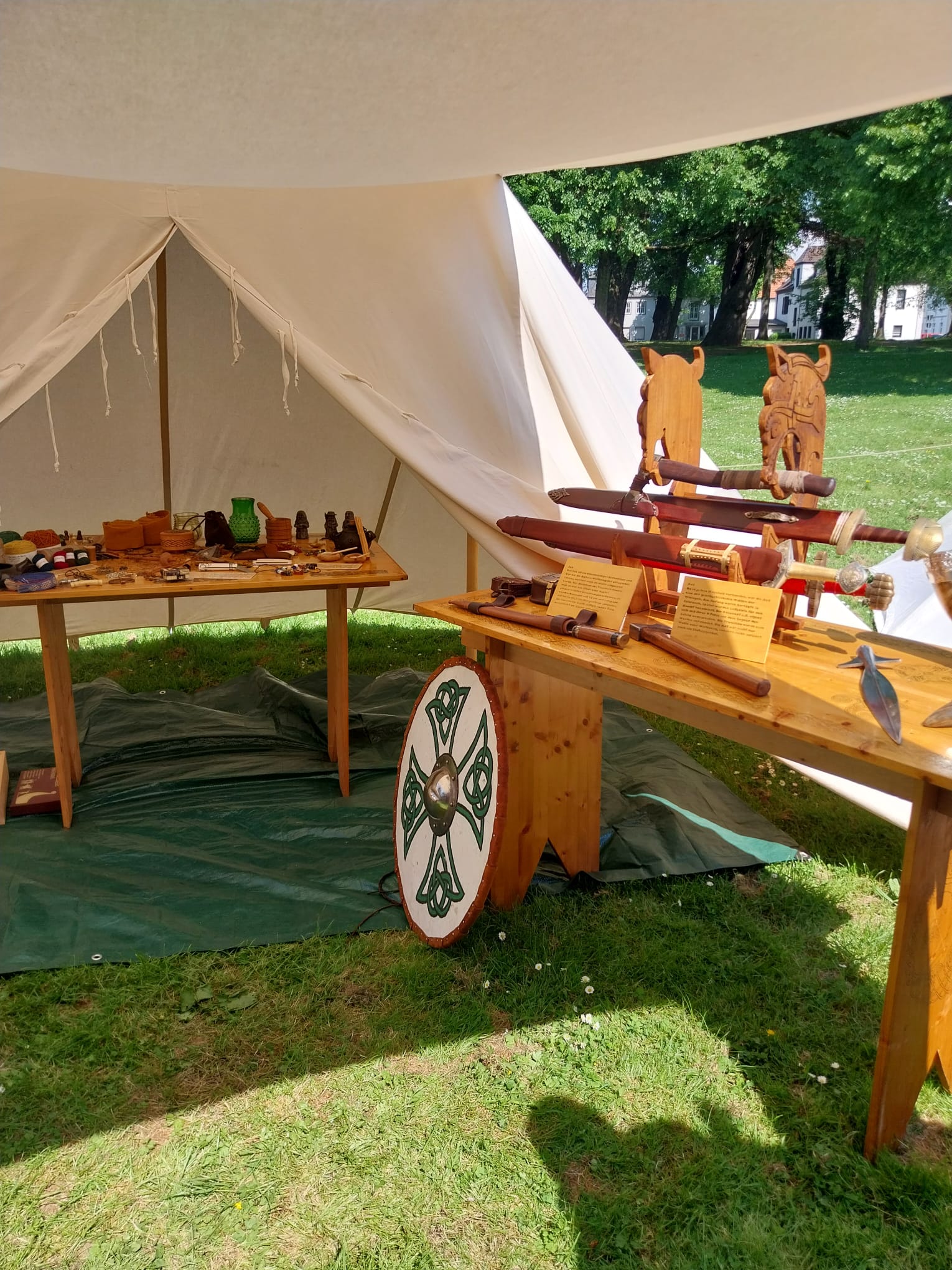 Im Museumszelt: der Waffentisch — Schwertständer mit Tierkopf-Pfosten, Äxten, Speerspitze und Schild