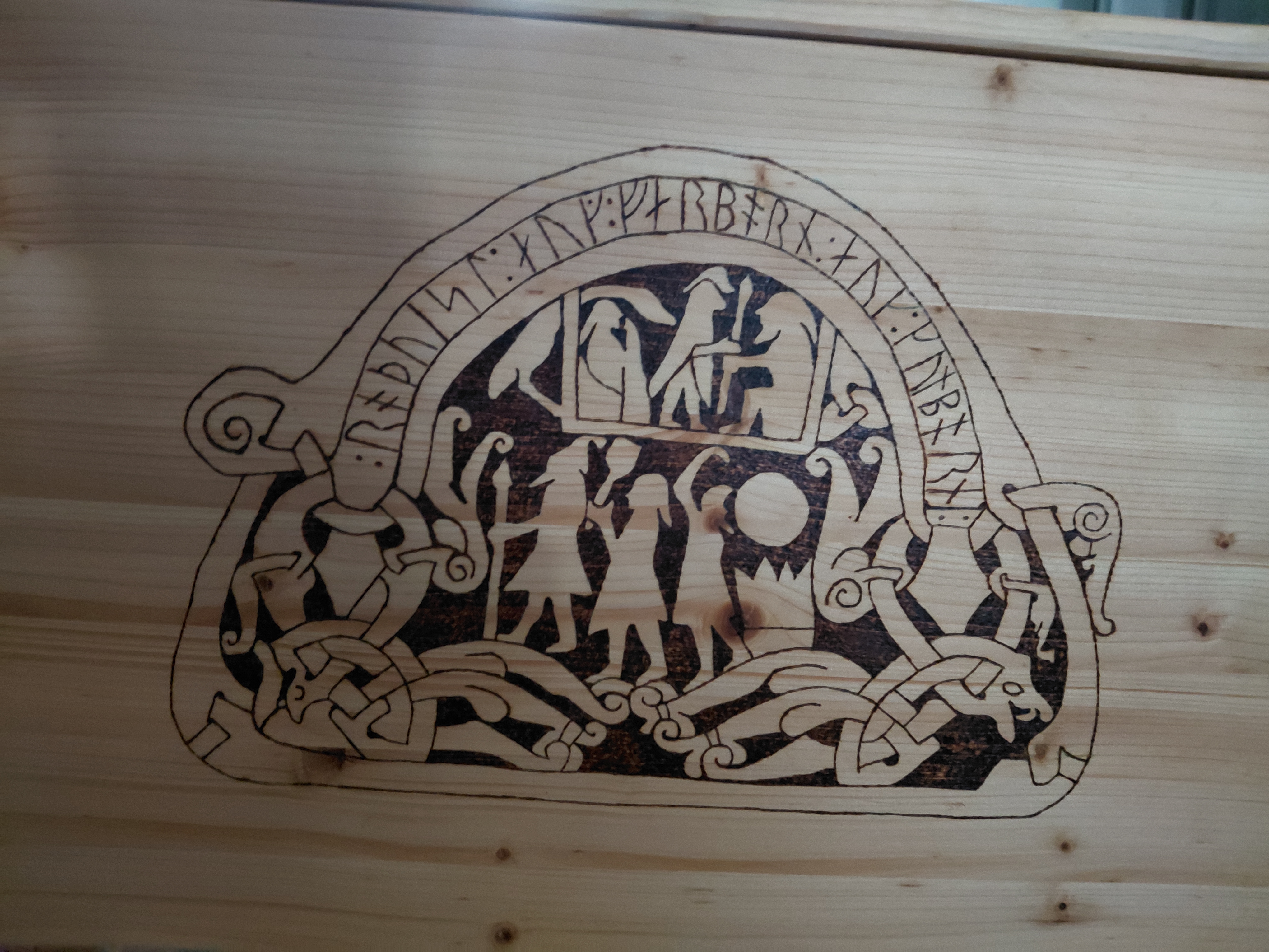 Unsere Truhen-Brandmalerei: Runenstein Sanda kyrka I (G 181) — gerahmte Szene mit Vogel, Figurenzug und Flechtwerk unter dem Runenband